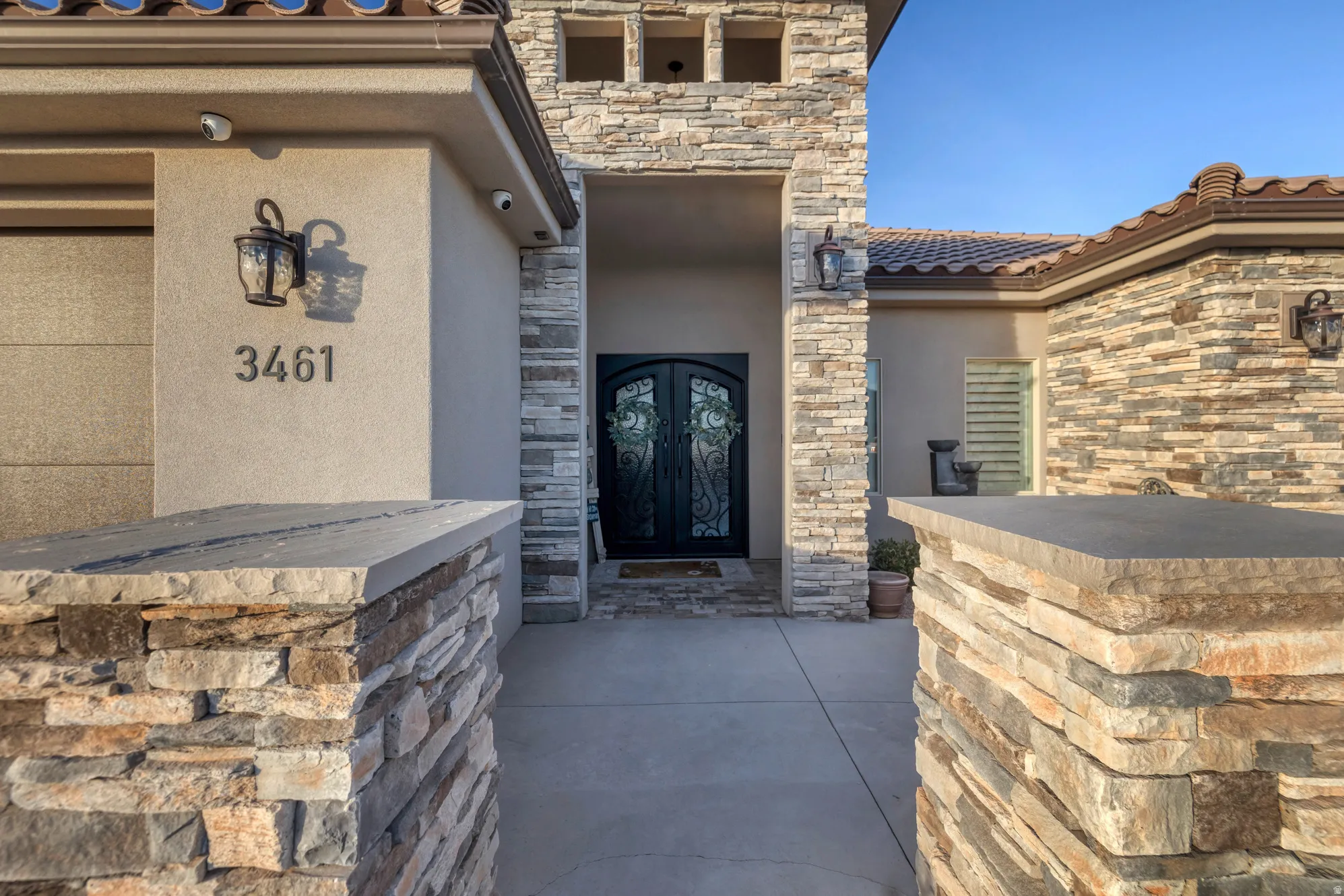 Stone facade with arched entry door, decorative sconce lighting, and a tiled roof
