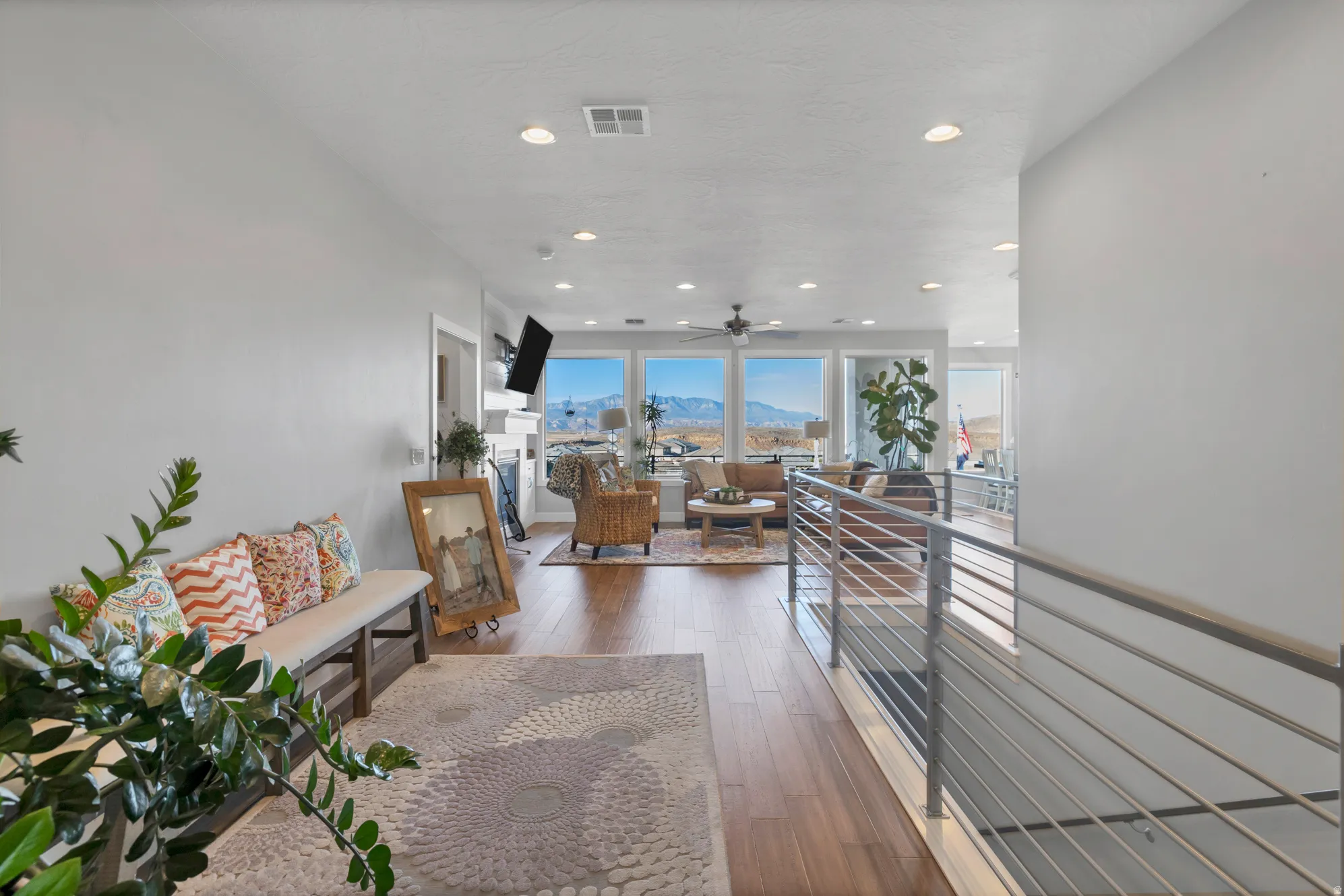 Open-concept layout with wood-finish flooring, recessed lighting, and a modern horizontal bar railing