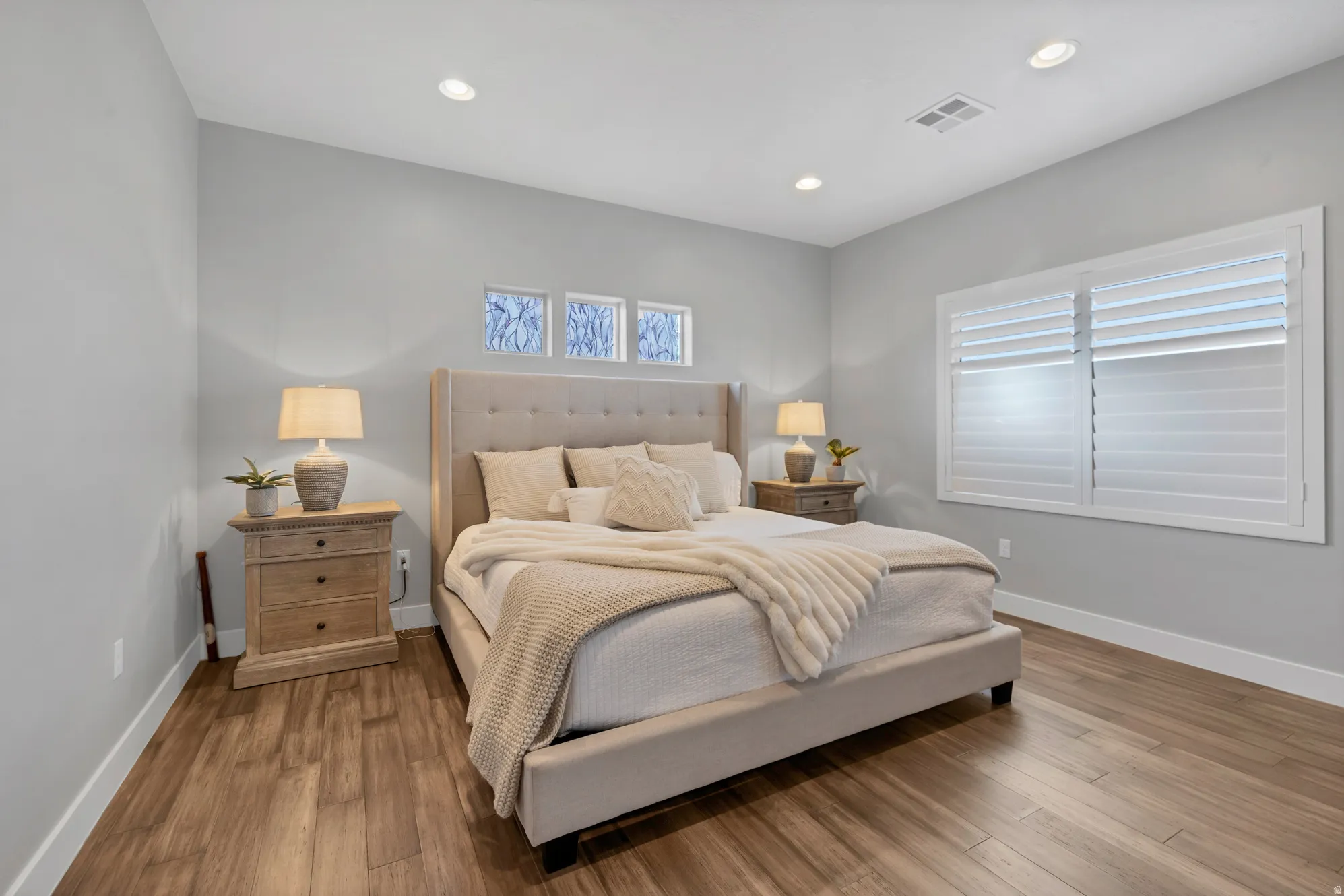 Wood-finish flooring with white baseboards, recessed lighting, and a window with plantation shutters