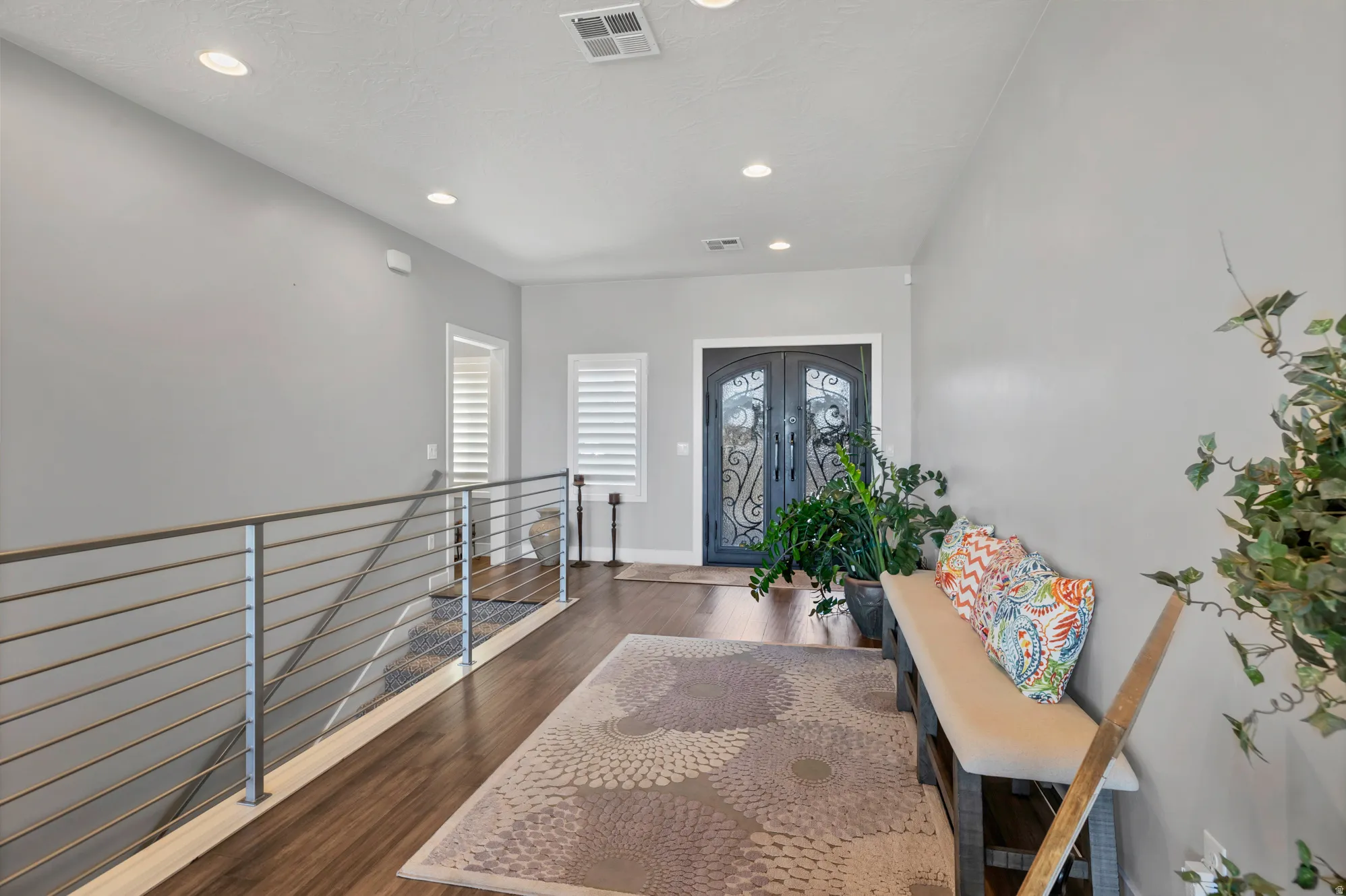 Double entry doors with decorative ironwork, wood-finish flooring, recessed lighting, and a metal horizontal bar railing system