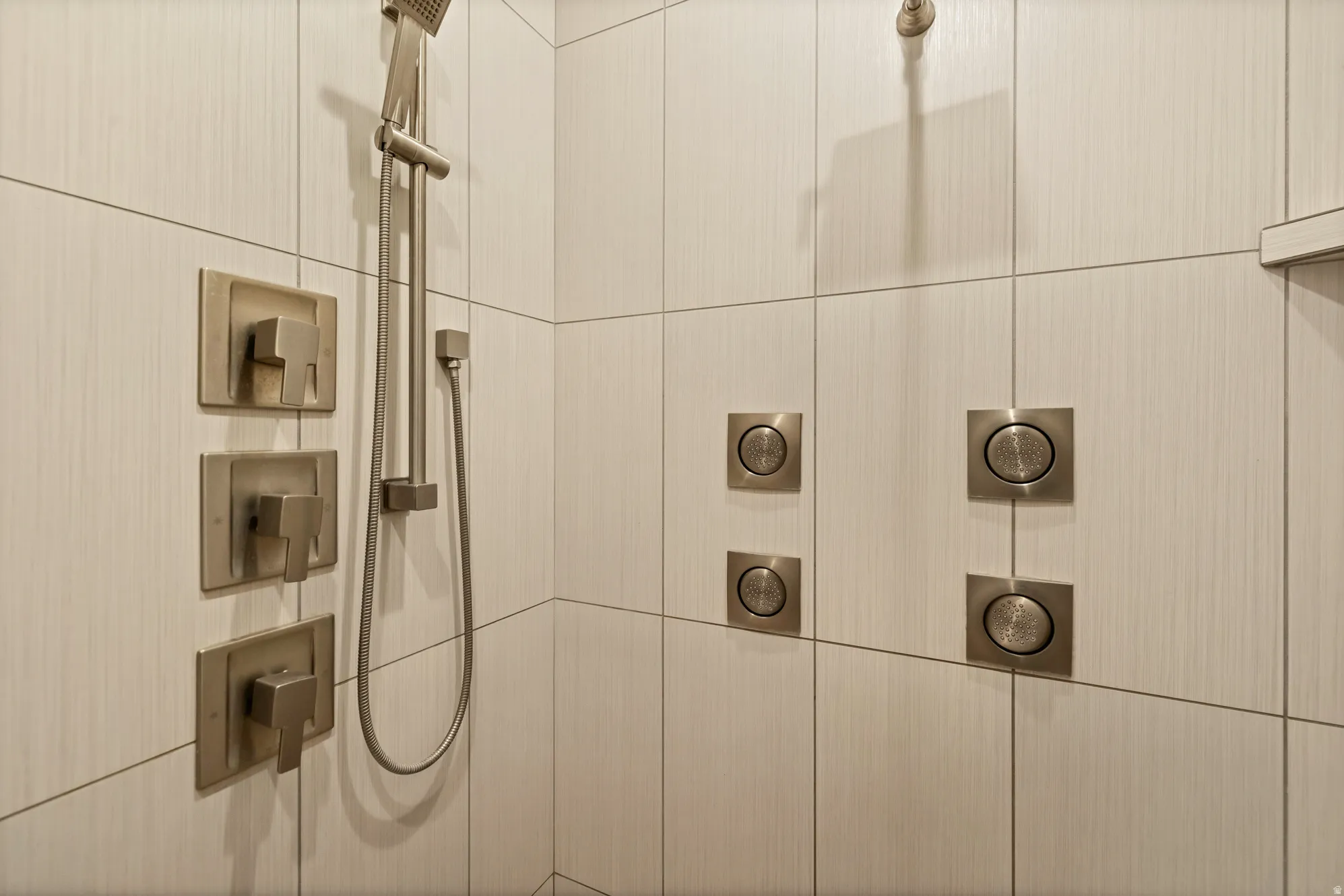 Tiled shower enclosure featuring a handheld showerhead, multiple body sprayers, and brushed nickel fixtures