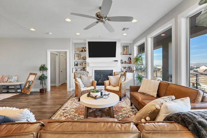 Living area featuring wood-finish flooring, recessed lighting, a ceiling fan, a fireplace with a white mantel, and built-in shelving