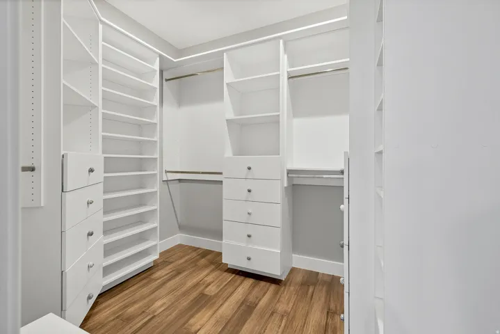 Custom closet system featuring white cabinetry, multiple shelving units, integrated drawers with metal pulls, and wood-finish flooring