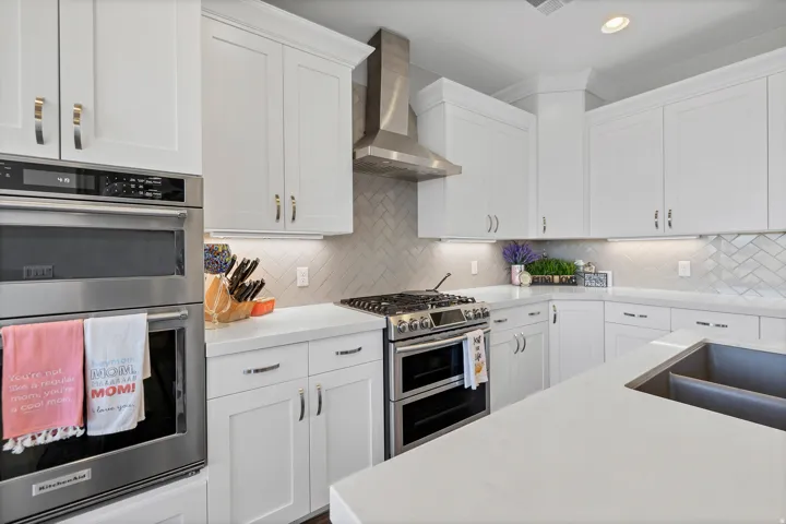 White shaker-style cabinetry, stainless steel appliances, quartz countertops, herringbone tile backsplash, and an undermount double basin sink