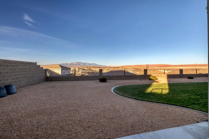 Expansive backyard featuring a concrete block retaining wall, gravel landscaping, a curved lawn area, and a perimeter fence