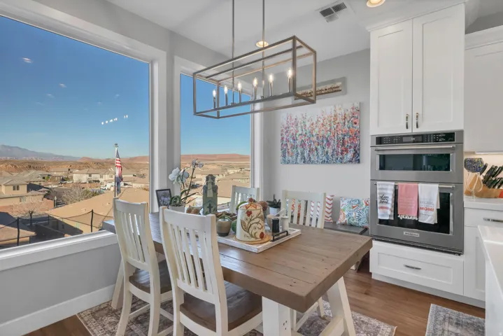 Built-in stainless steel double oven, white shaker-style cabinetry, wood-finish flooring, rectangular chandelier, and expansive windows
