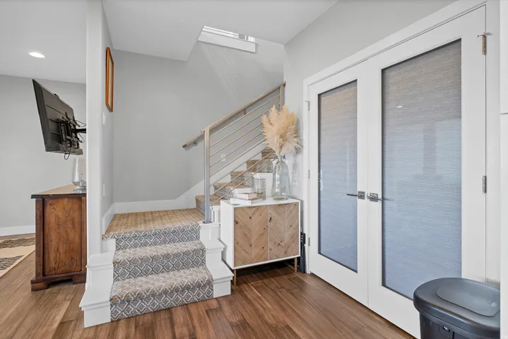 Wood-finish flooring, staircase with patterned carpet runner, contemporary cable railing, white French doors with frosted glass, recessed lighting