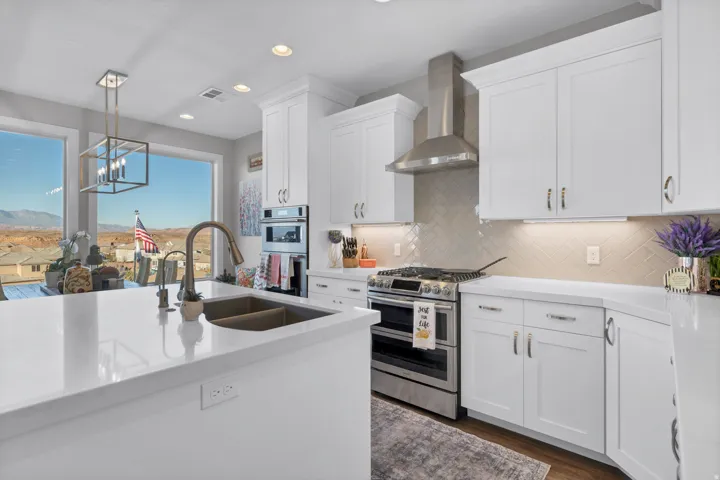 Kitchen featuring white shaker-style cabinetry, stainless steel appliances, a herringbone tile backsplash, and an island with an undermount sink