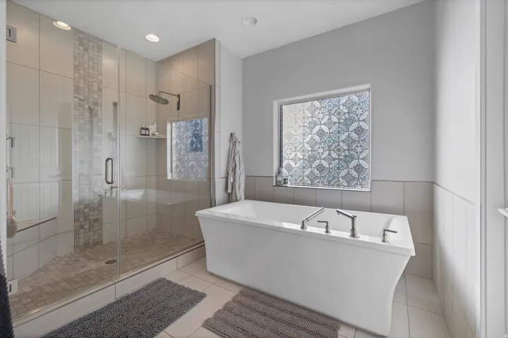 Freestanding soaking tub with chrome fixtures, glass-enclosed shower with tile surround, patterned window, and recessed lighting