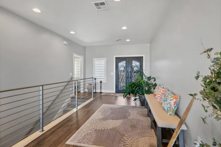 Double entry doors with decorative ironwork, wood-finish flooring, recessed lighting, and a metal horizontal bar railing system