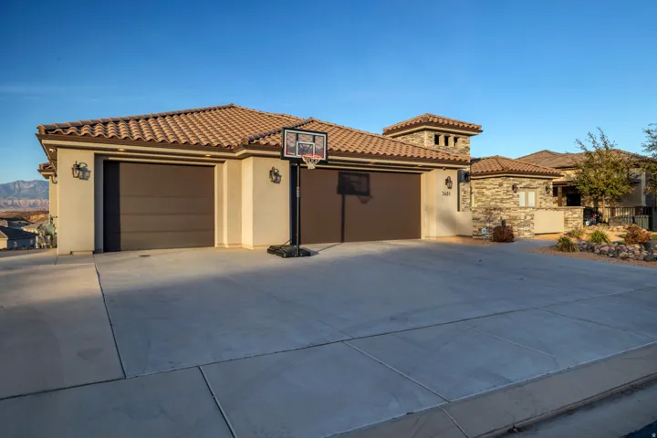 Stucco exterior with a tile roof, an integrated two-car garage, a concrete driveway, and stone accents