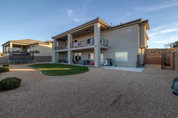 Multi-level stucco exterior with covered patios, upper balcony with metal railings, and a landscaped yard featuring gravel and a shaped lawn