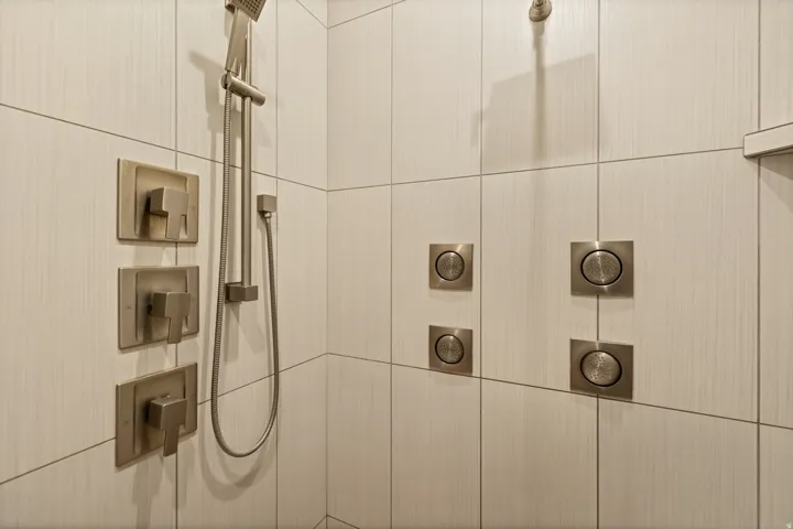 Tiled shower enclosure featuring a handheld showerhead, multiple body sprayers, and brushed nickel fixtures