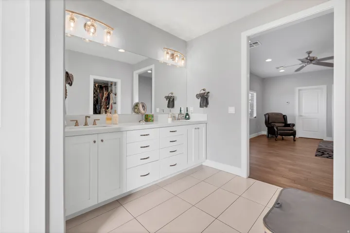 Dual vanity with white cabinetry, gold-finish hardware, and a large wall-mounted mirror