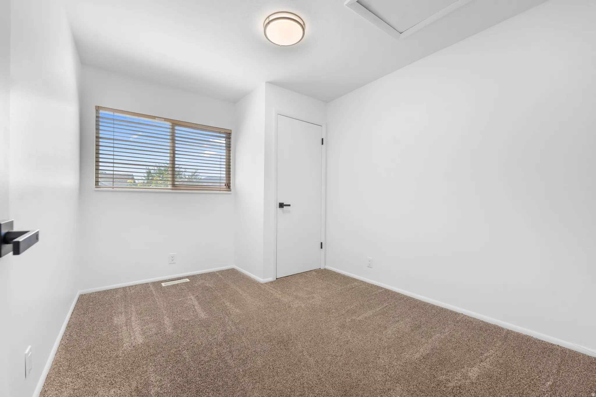 Neutral-toned carpeting, white walls, horizontal window blinds, and a flush-mount ceiling light fixture