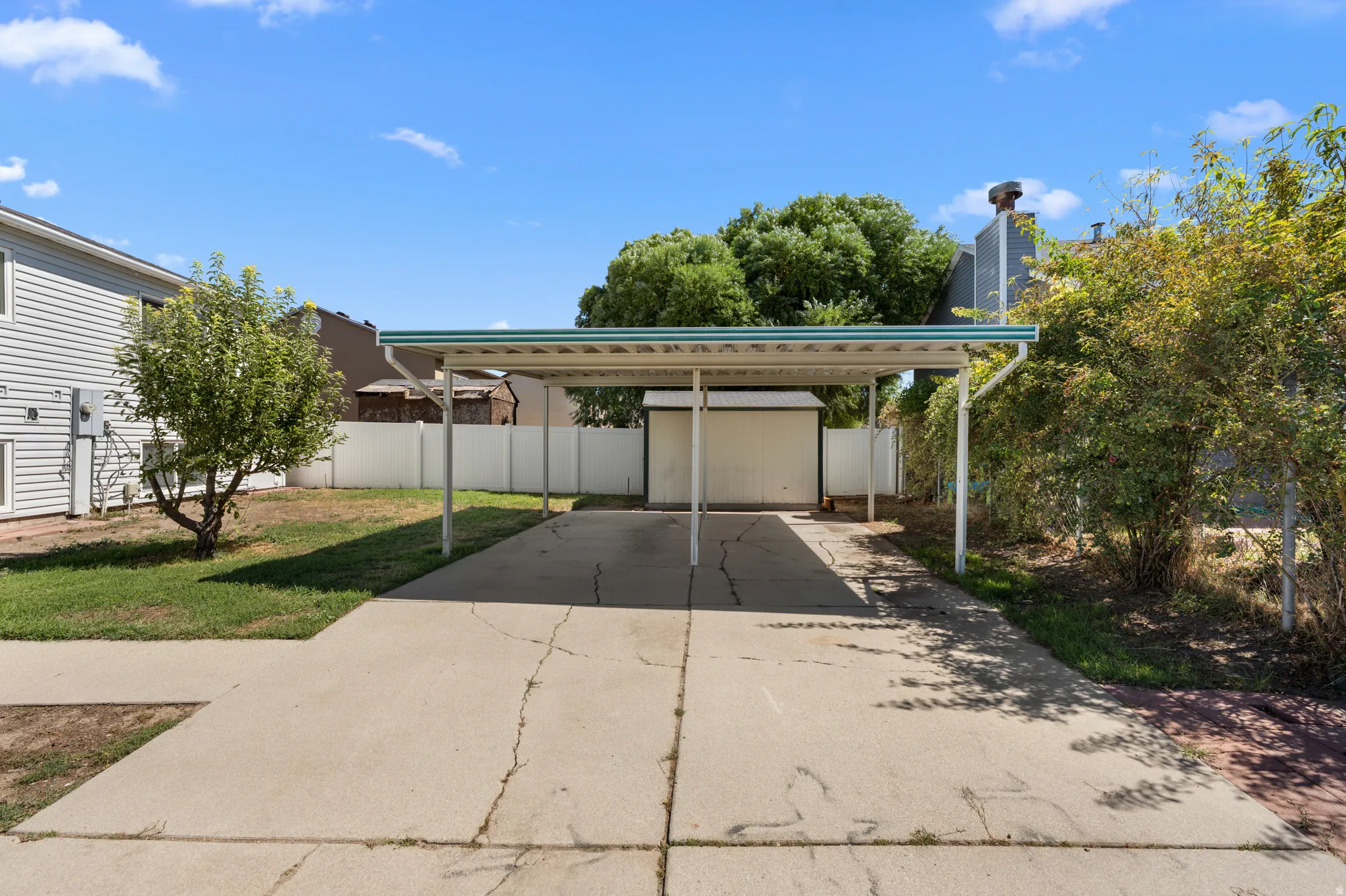 Concrete driveway with a covered carport, leading to a detached storage shed