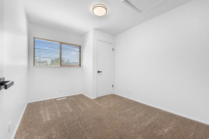 Neutral-toned carpeting, white walls, horizontal window blinds, and a flush-mount ceiling light fixture