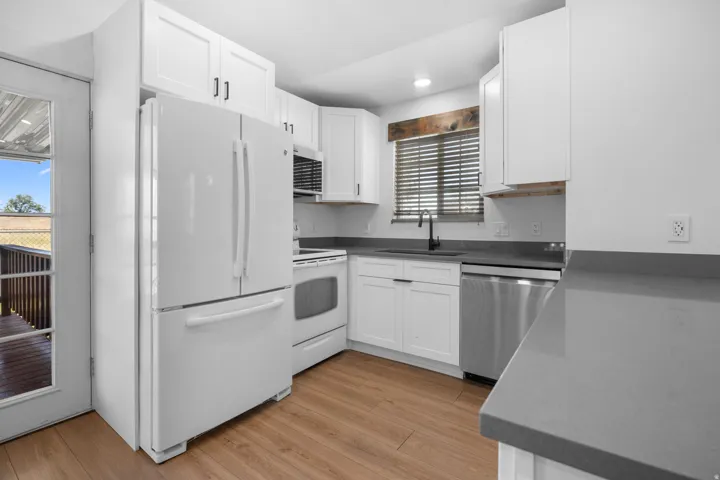 Modern kitchen featuring white shaker-style cabinetry, a built-in microwave, laminate flooring, and quartz countertops