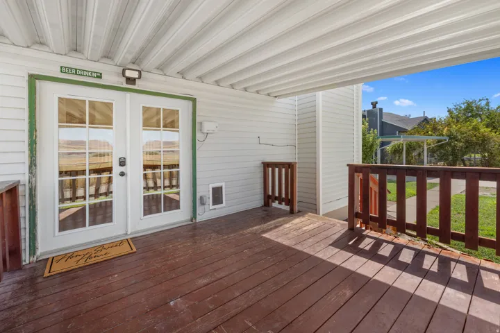 Covered wood-finish patio featuring wood-finish railings, white siding, and French doors with grid-patterned glass