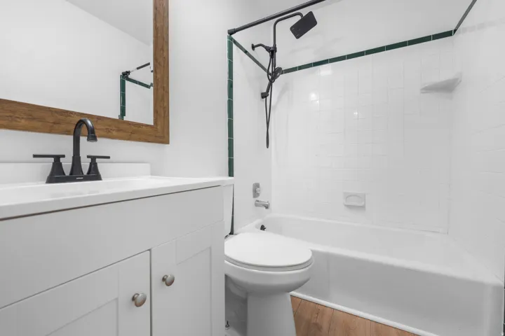 White vanity with a solid surface countertop and matte black faucet, full bathtub with a wall-mounted shower system, white subway tile surround.