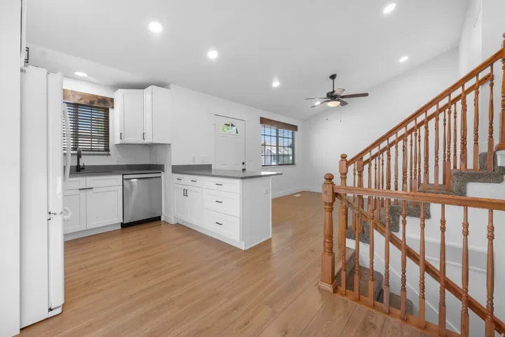 White cabinetry with dark hardware, stainless steel dishwasher, laminate flooring, and a wooden staircase with carpeted treads