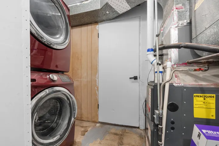 Laundry area featuring a stackable washer and dryer, utility door, and HVAC system, tankless water heater, water softener.