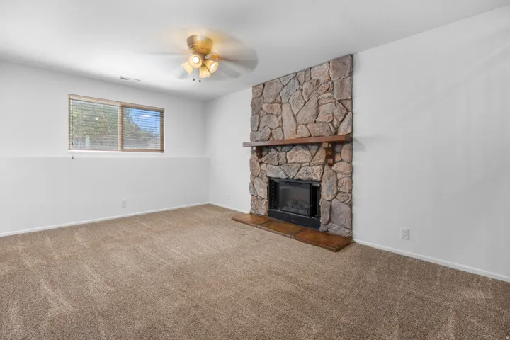 Stone-clad fireplace with wood mantle and hearth, ceiling fan, and carpeted flooring