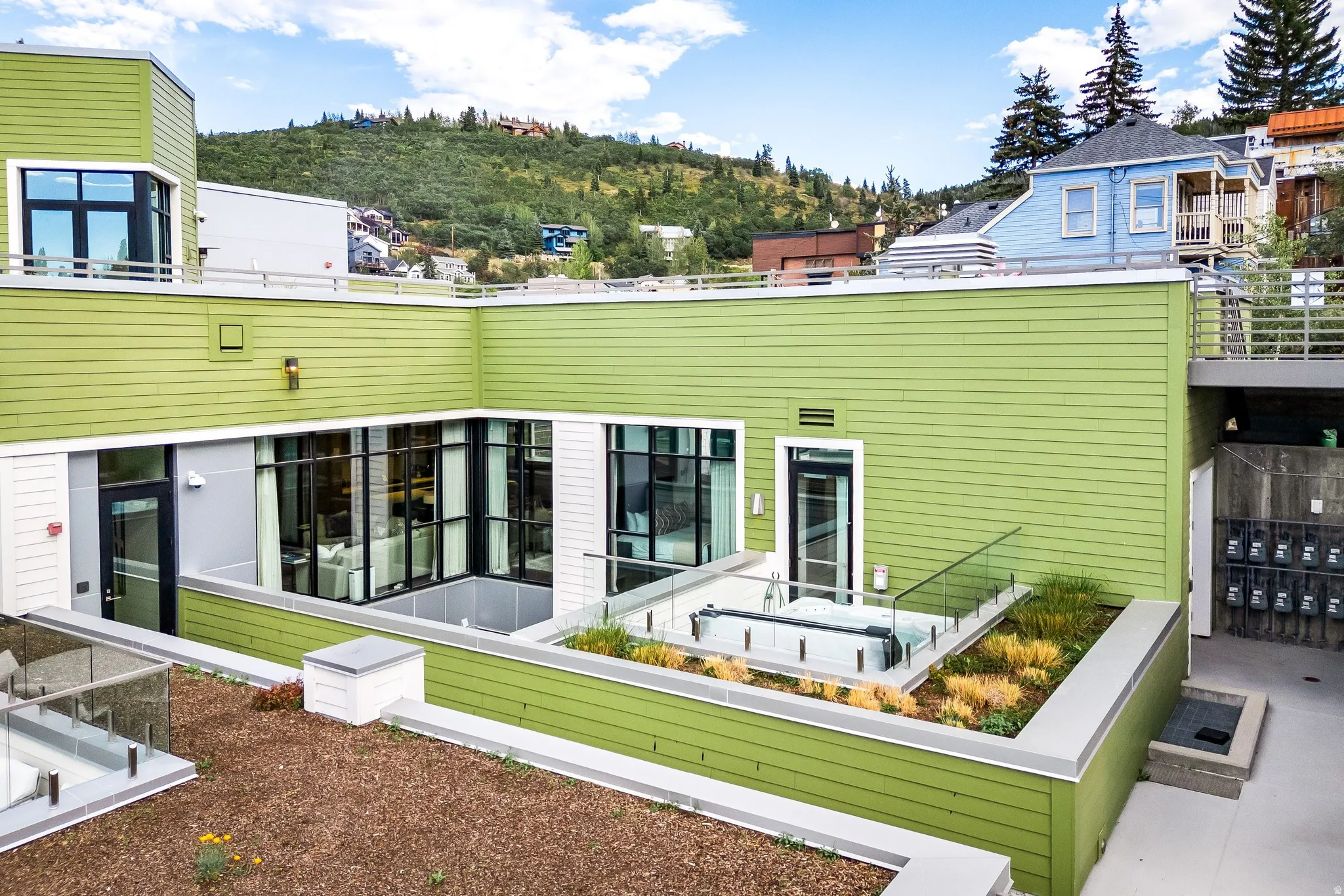 Modern facade with green siding, expansive glass windows, and glass railings