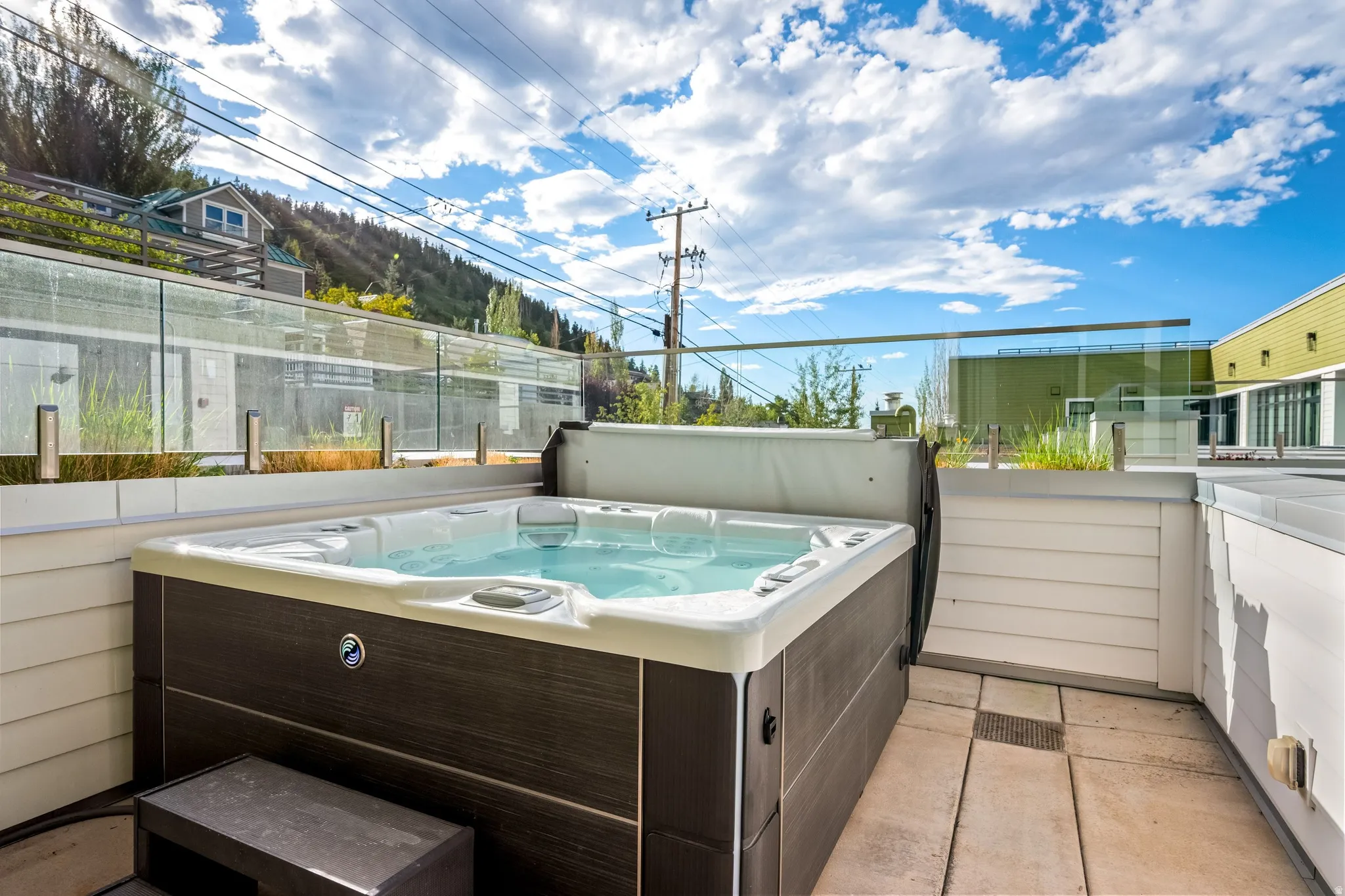 Private patio featuring a built-in hot tub, glass railing, and neutral-toned hardscaping