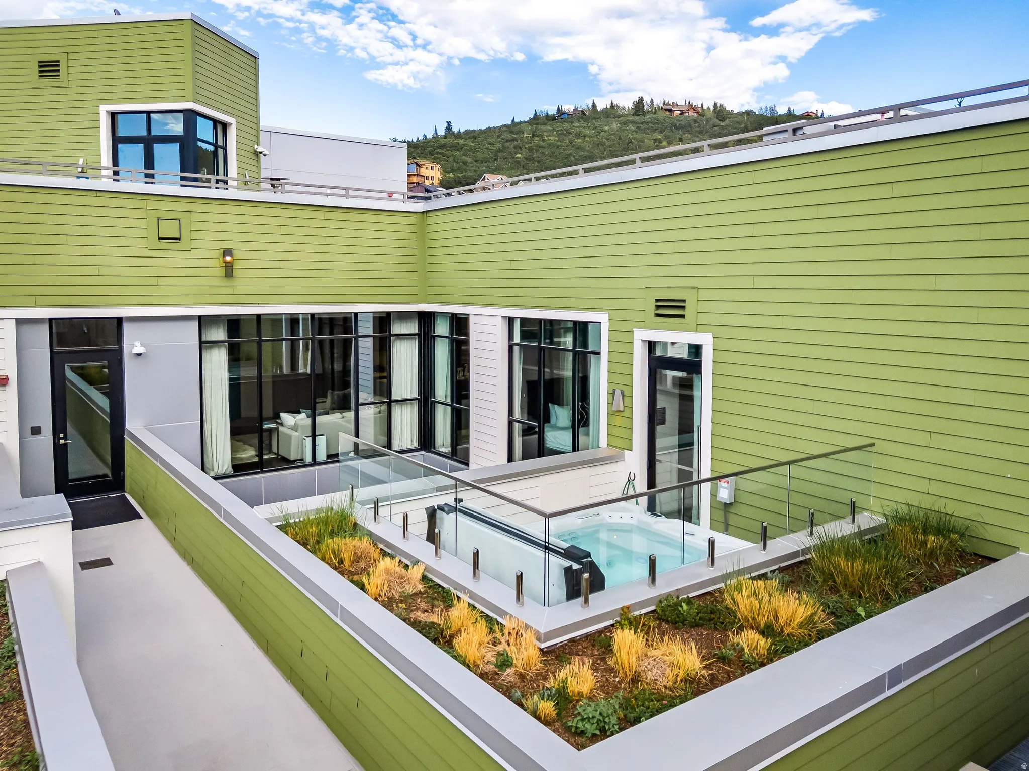 Private outdoor terrace featuring an in-ground spa, glass railing, and integrated landscaping