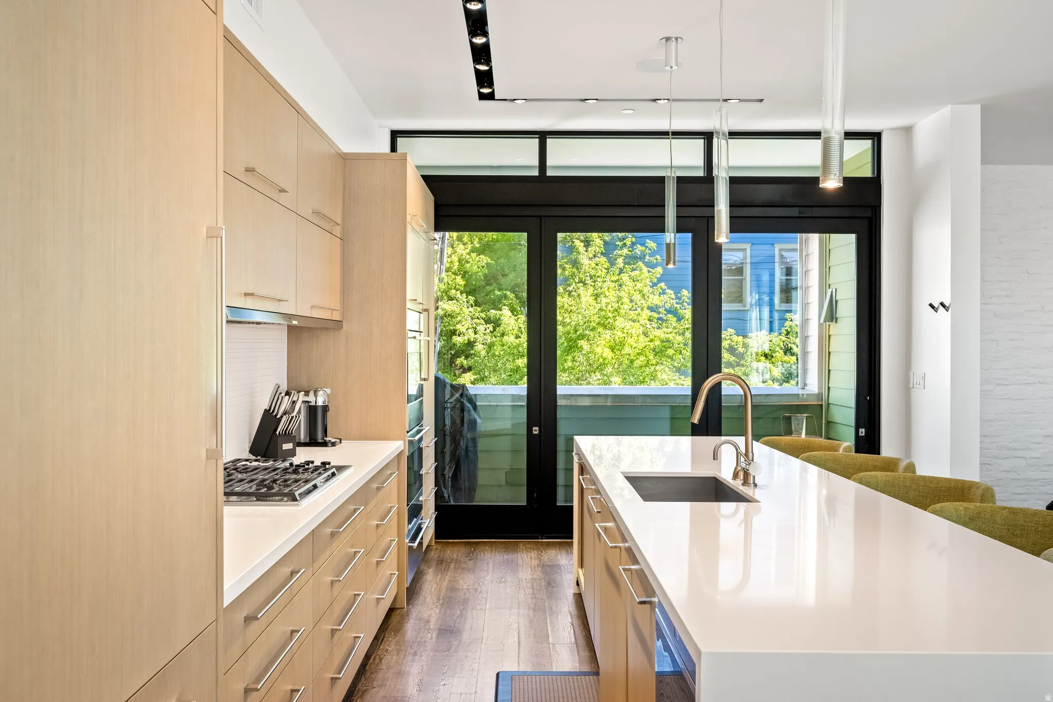 Kitchen with light wood-finish cabinetry, built-in appliances, a gas range, and a long white countertop with an integrated sink