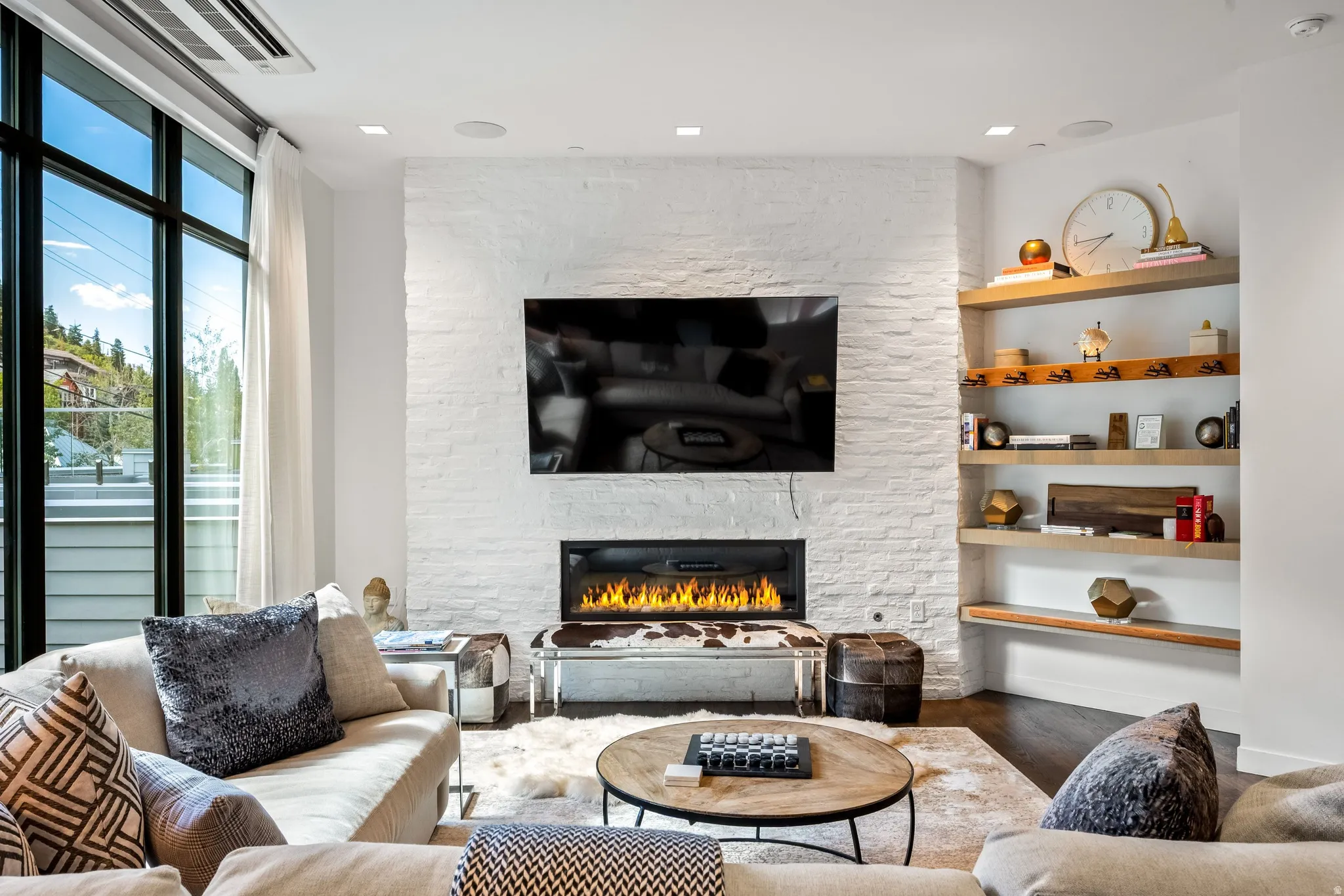 White brick fireplace with an integrated linear fire feature, dark wood-finish flooring, built-in open shelving, and large multi-pane windows
