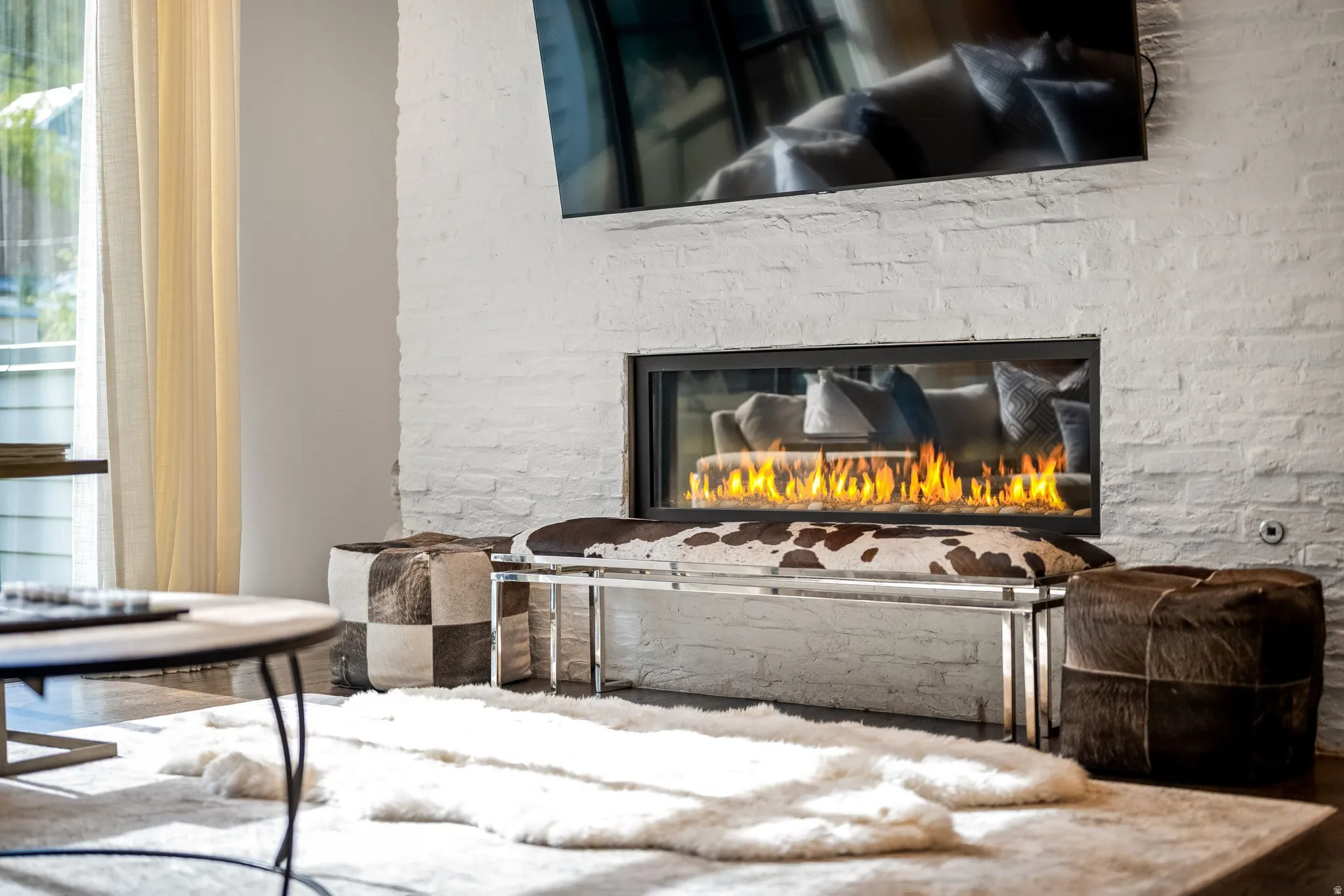White brick accent wall with a linear fireplace, dark wood-finish flooring, and a large window