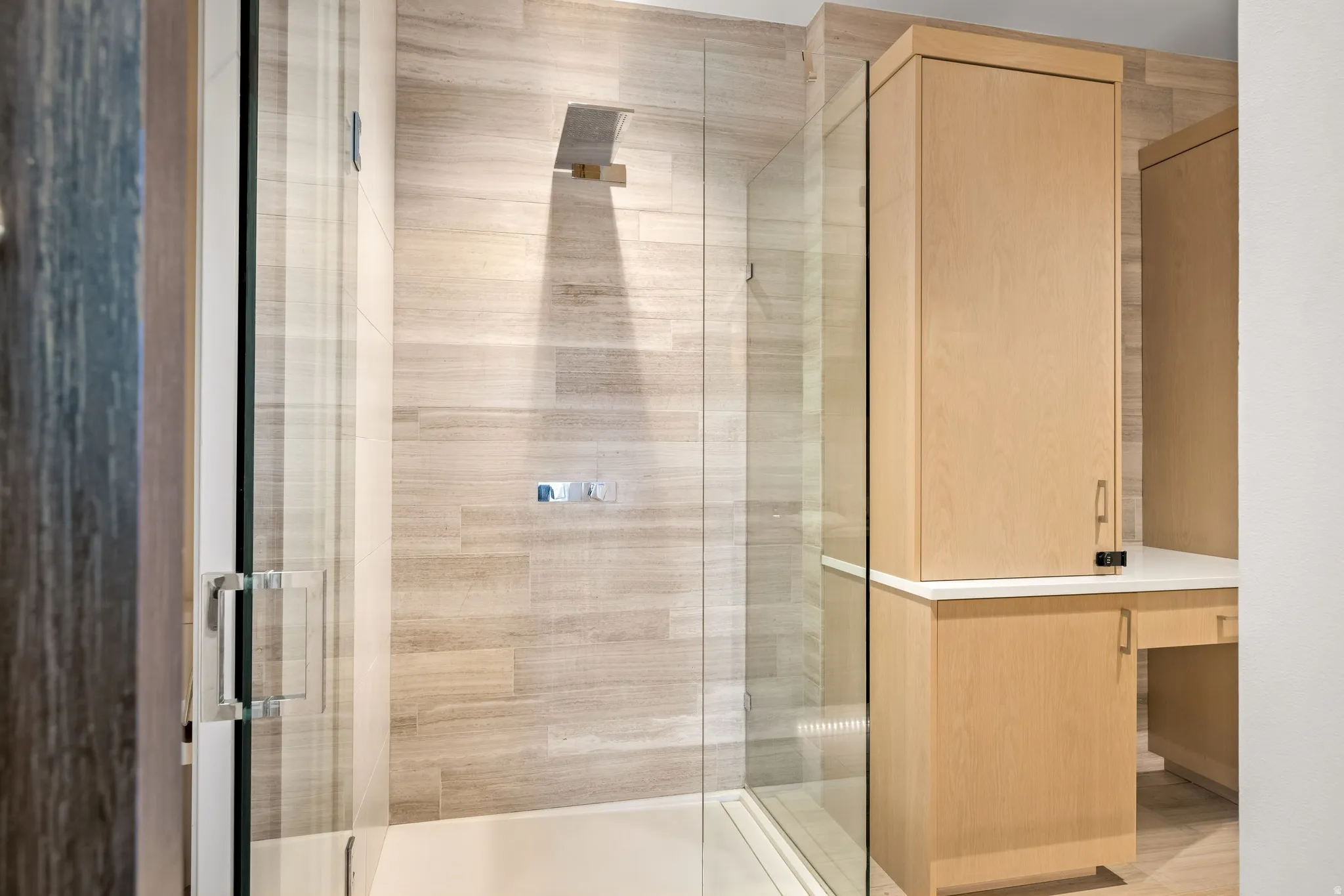 Glass-enclosed shower with a rainfall showerhead, large format wall tile, and integrated shower controls
