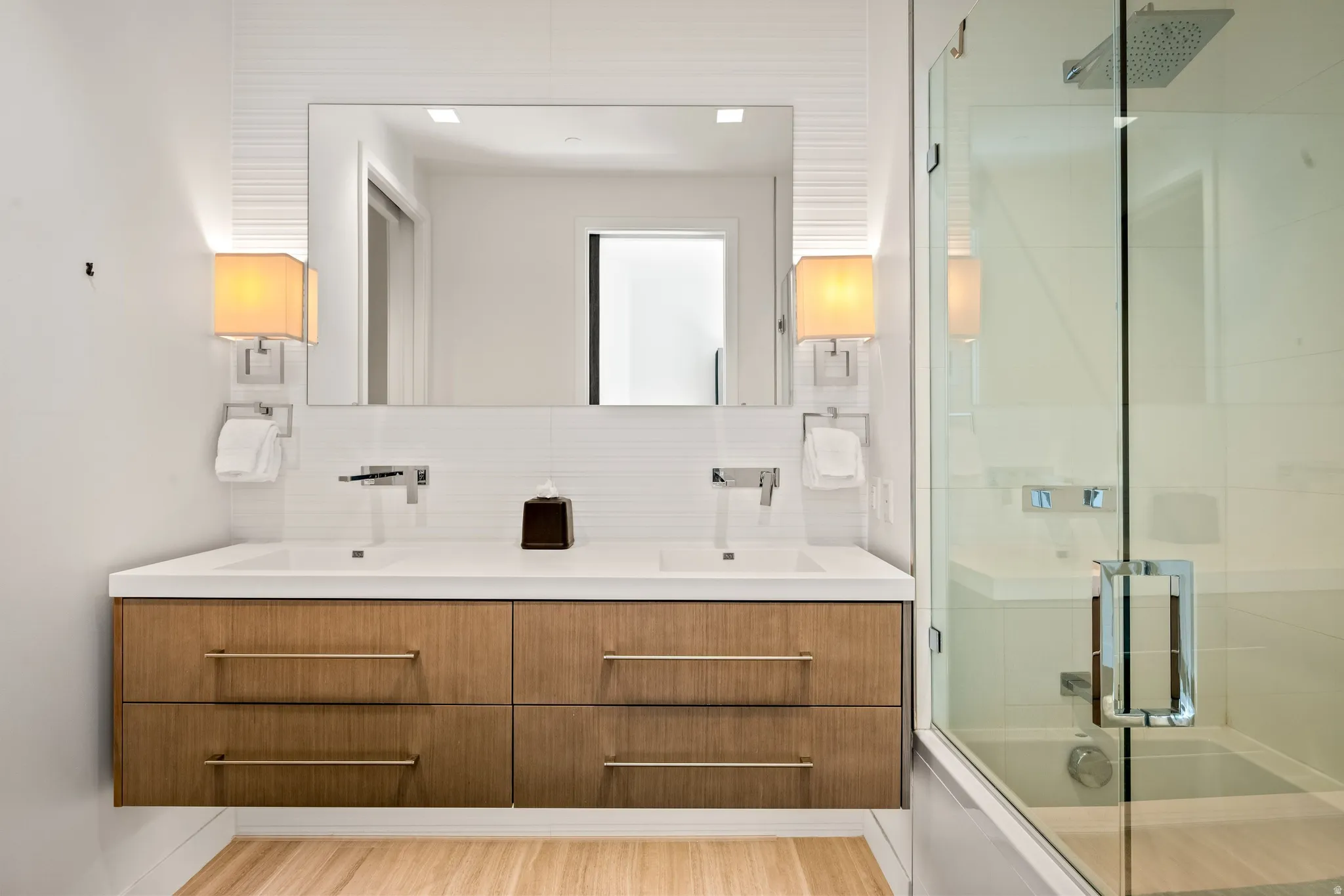 Floating wood-finish vanity with dual integrated sinks, chrome fixtures, and a large wall-mounted mirror