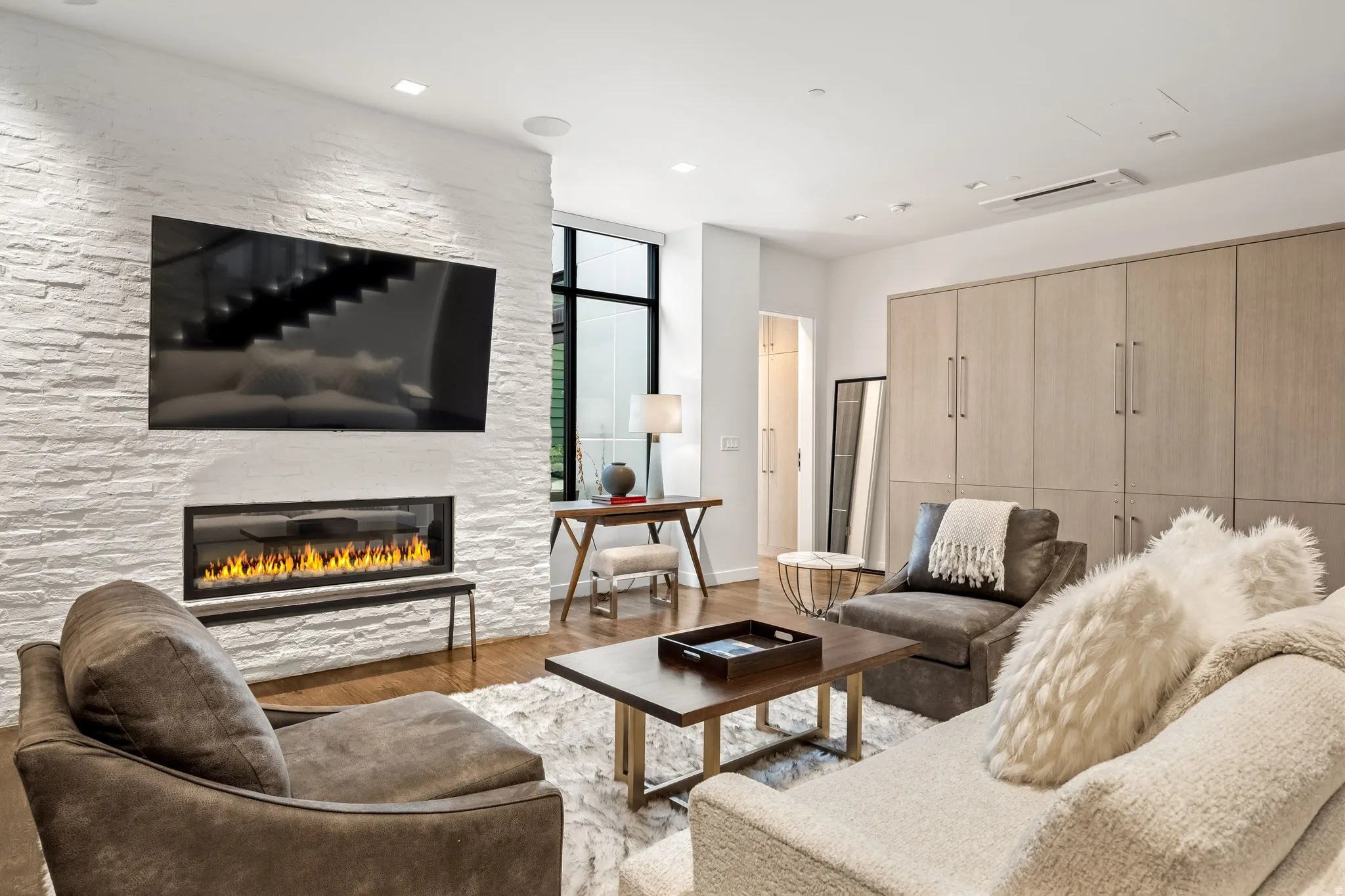 Stacked stone accent wall with a linear fireplace, recessed lighting, wood-finish flooring, and integrated cabinetry