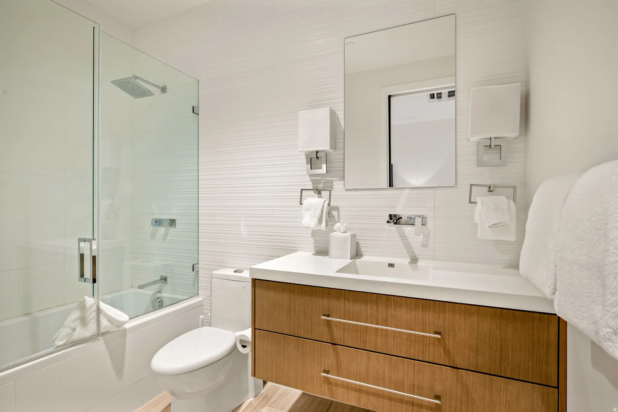 Wood-finish vanity with an integrated sink, polished chrome fixtures, and a frameless mirror