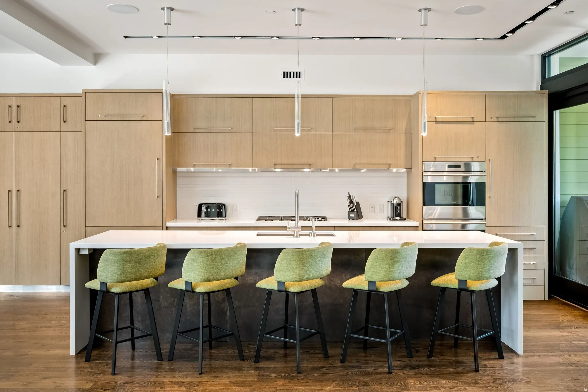 Kitchen featuring wood-finish cabinetry, integrated appliances, a waterfall island with seating, a white tile backsplash, and recessed and pendant lighting