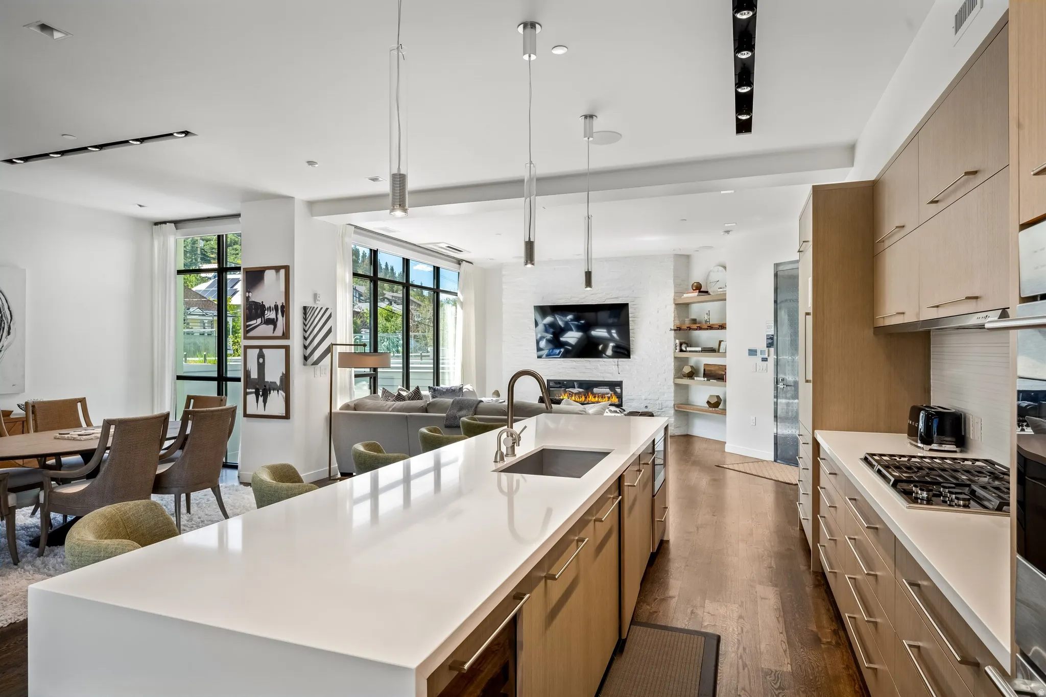 Open-concept living space with wood-finish flooring, a kitchen island with integrated sink, modern pendant lighting, extensive built-in cabinetry, and a gas cooktop