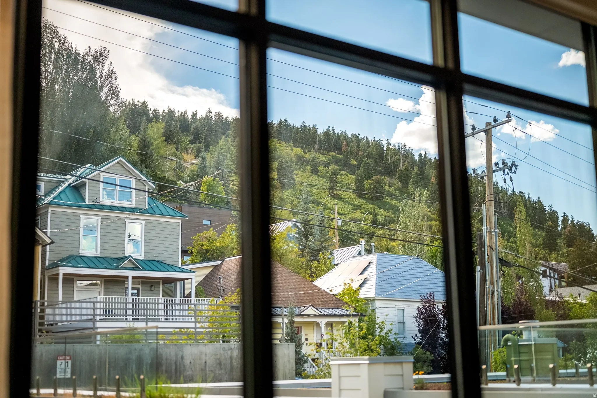Expansive window framing, hillside views, mature trees, residential structures