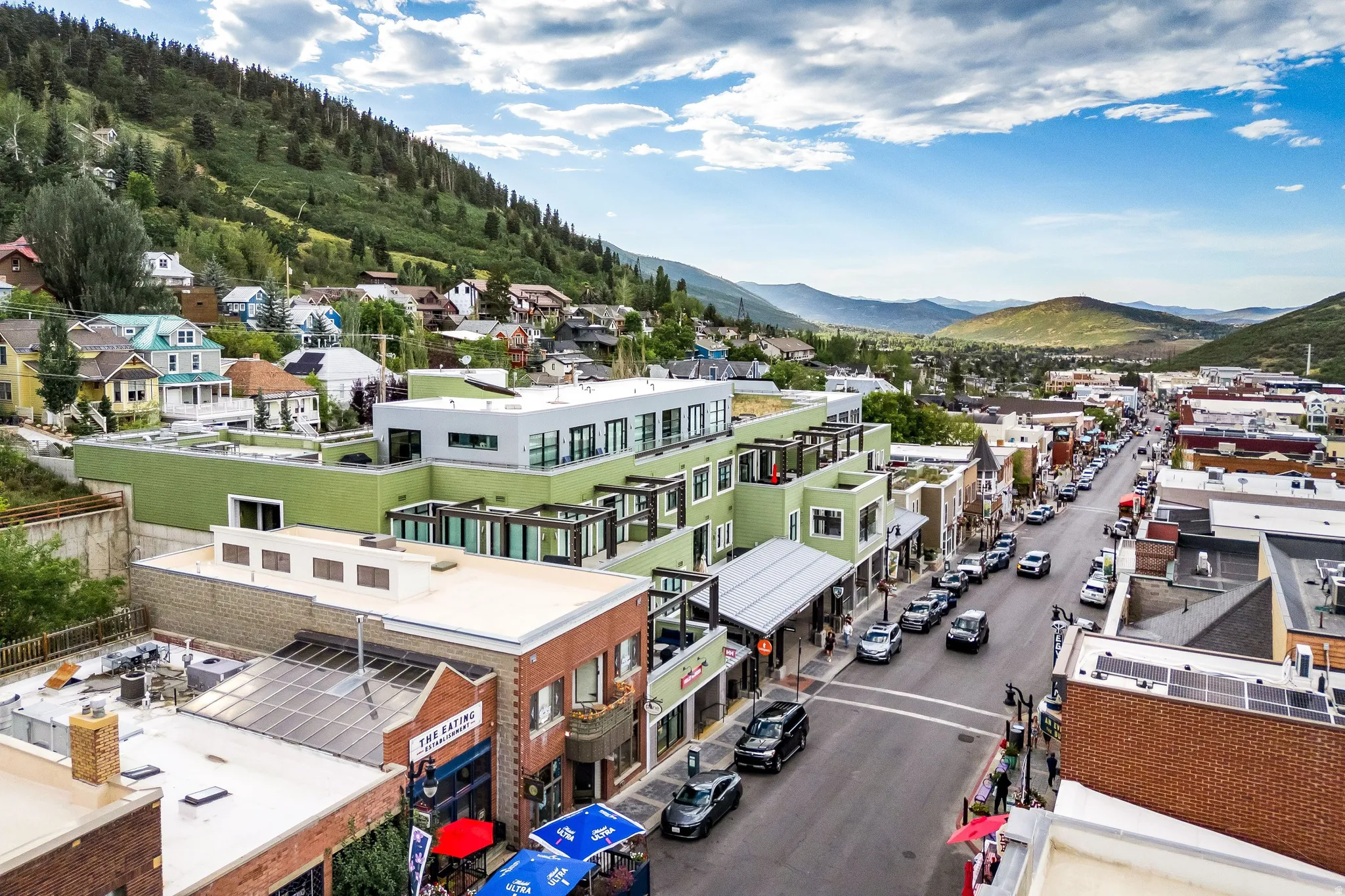 Mountainous terrain backdrop, varied residential architecture, commercial street frontage, diverse commercial buildings, clear sky with clouds