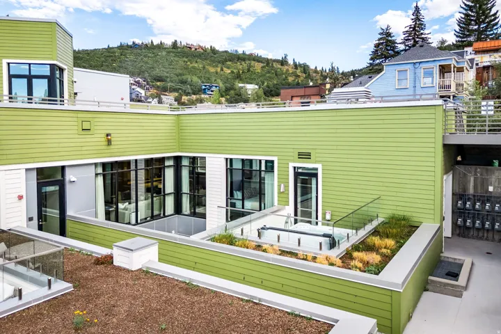 Modern facade with green siding, expansive glass windows, and glass railings