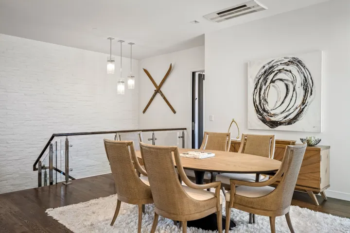 White painted brick accent wall, sleek glass and metal staircase railing, dark wood-finish flooring, contemporary pendant lighting, and a built-in wood credenza