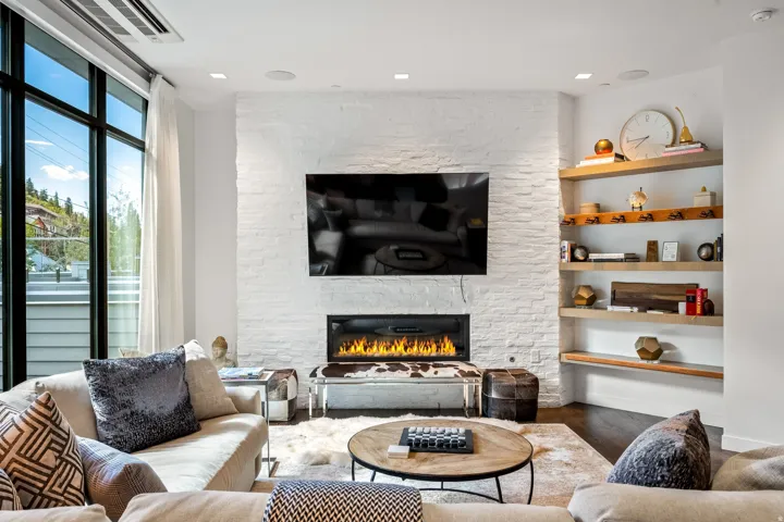 White brick fireplace with an integrated linear fire feature, dark wood-finish flooring, built-in open shelving, and large multi-pane windows