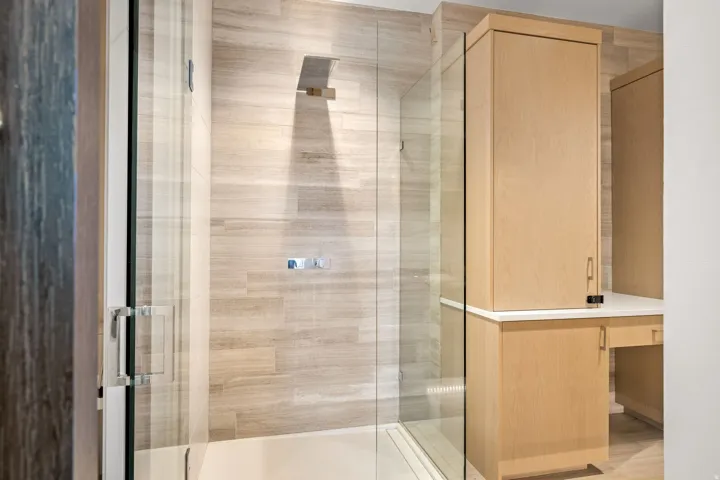 Glass-enclosed shower with a rainfall showerhead, large format wall tile, and integrated shower controls