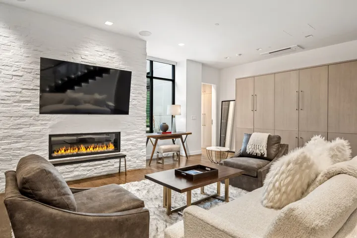 Stacked stone accent wall with a linear fireplace, recessed lighting, wood-finish flooring, and integrated cabinetry