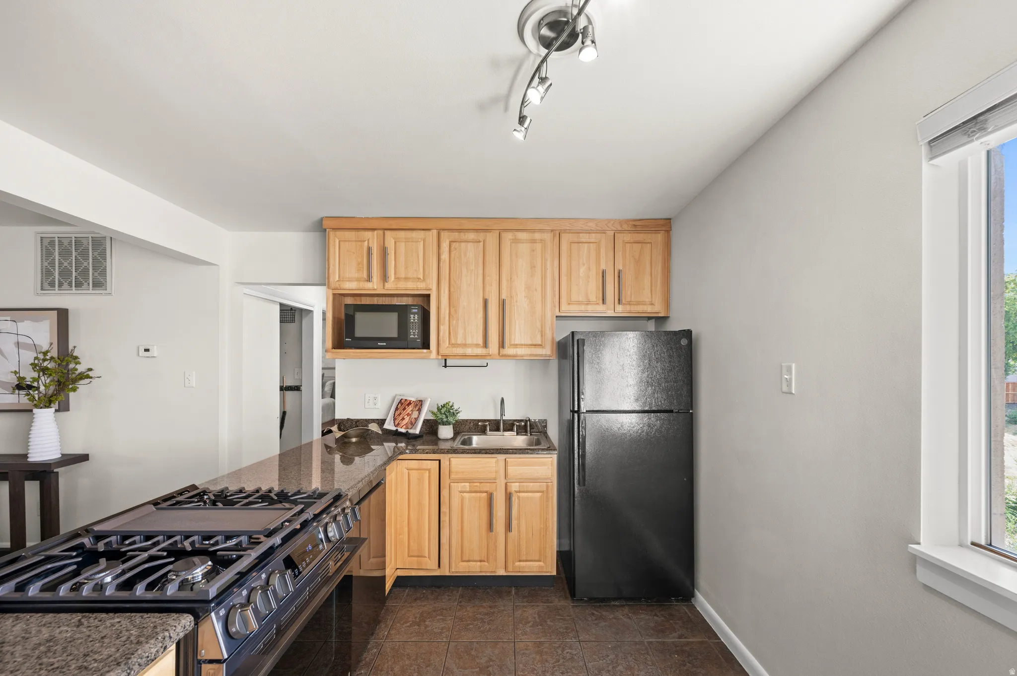 Kitchen featuring a built-in microwave, wood cabinetry, dark-finish appliances, track lighting, and a window