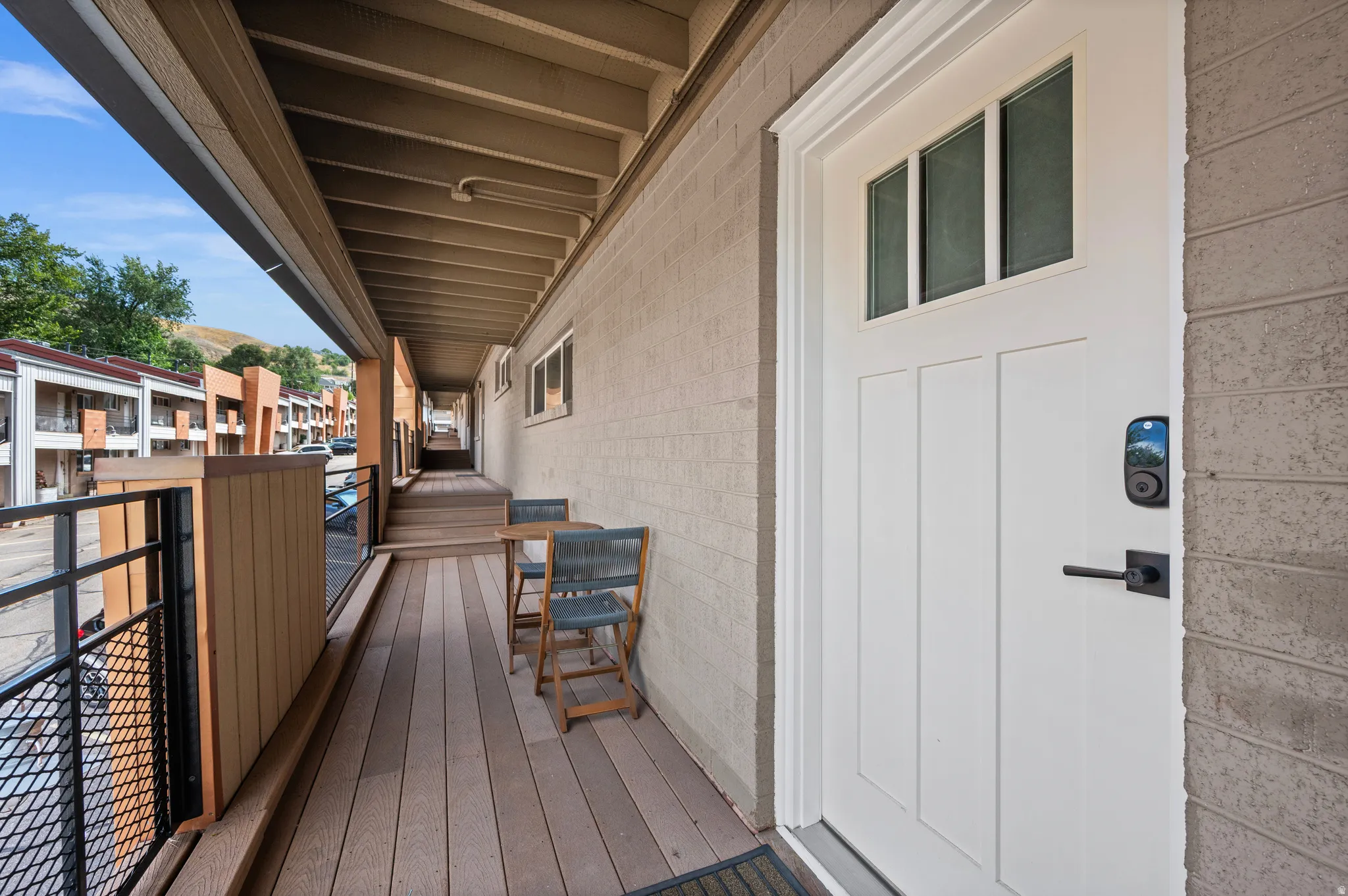 Expansive covered balcony featuring wood-finish flooring, a wood and metal railing, and a modern entry door with transom windows