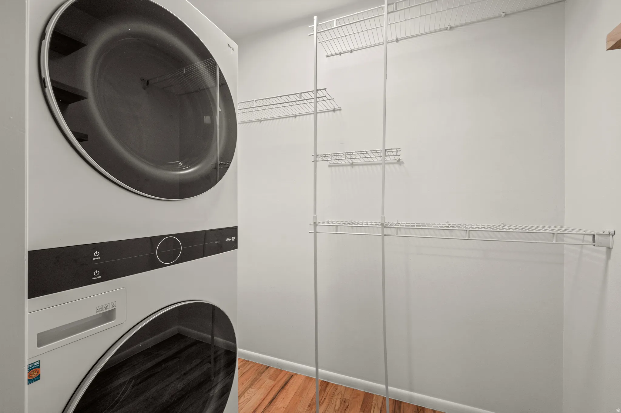 Stacked laundry appliances, wire shelving, and wood-finish flooring
