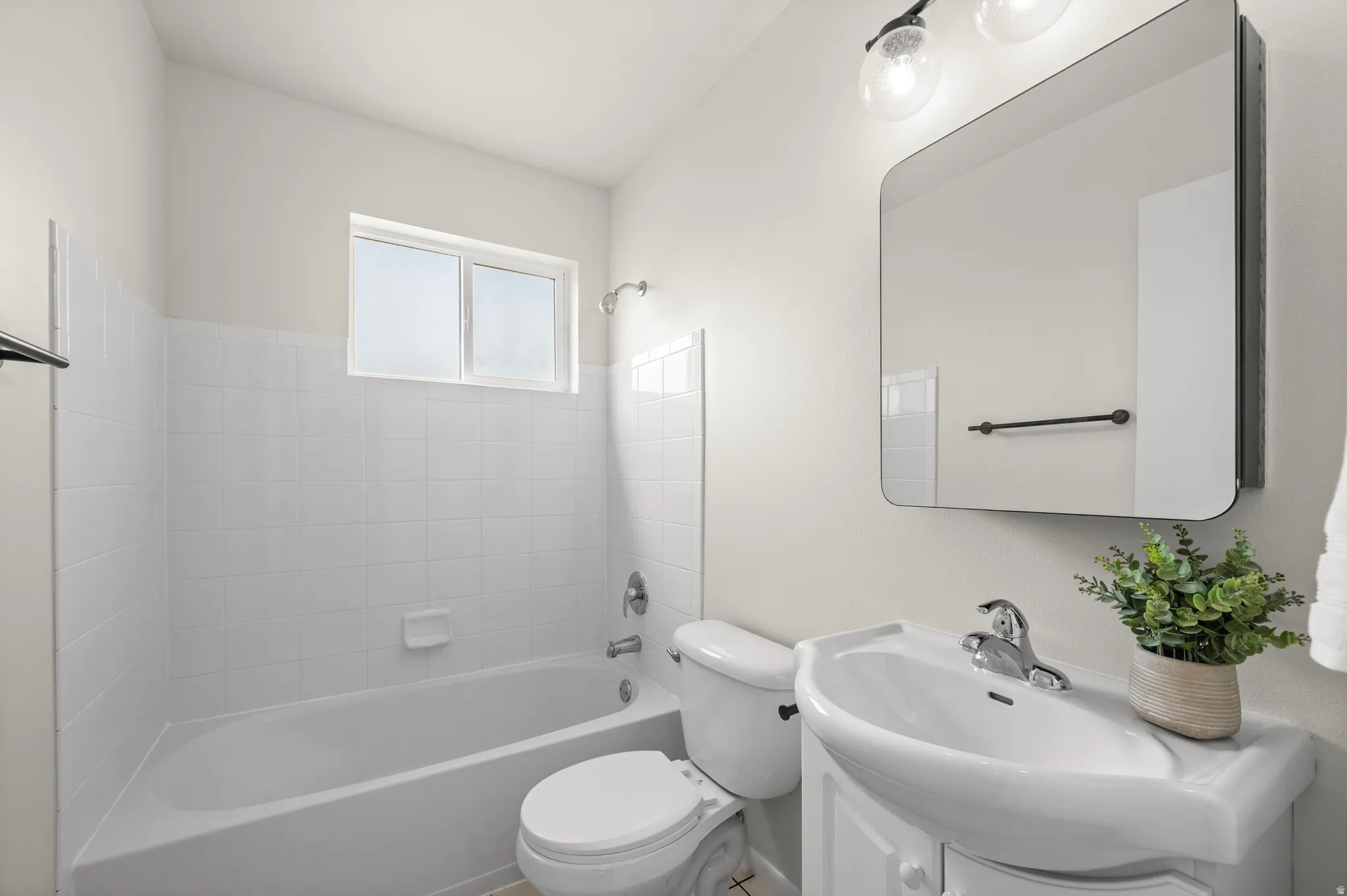 White ceramic tile tub surround with window, wall-mounted vanity with integrated sink, chrome faucet, and rectangular framed mirror